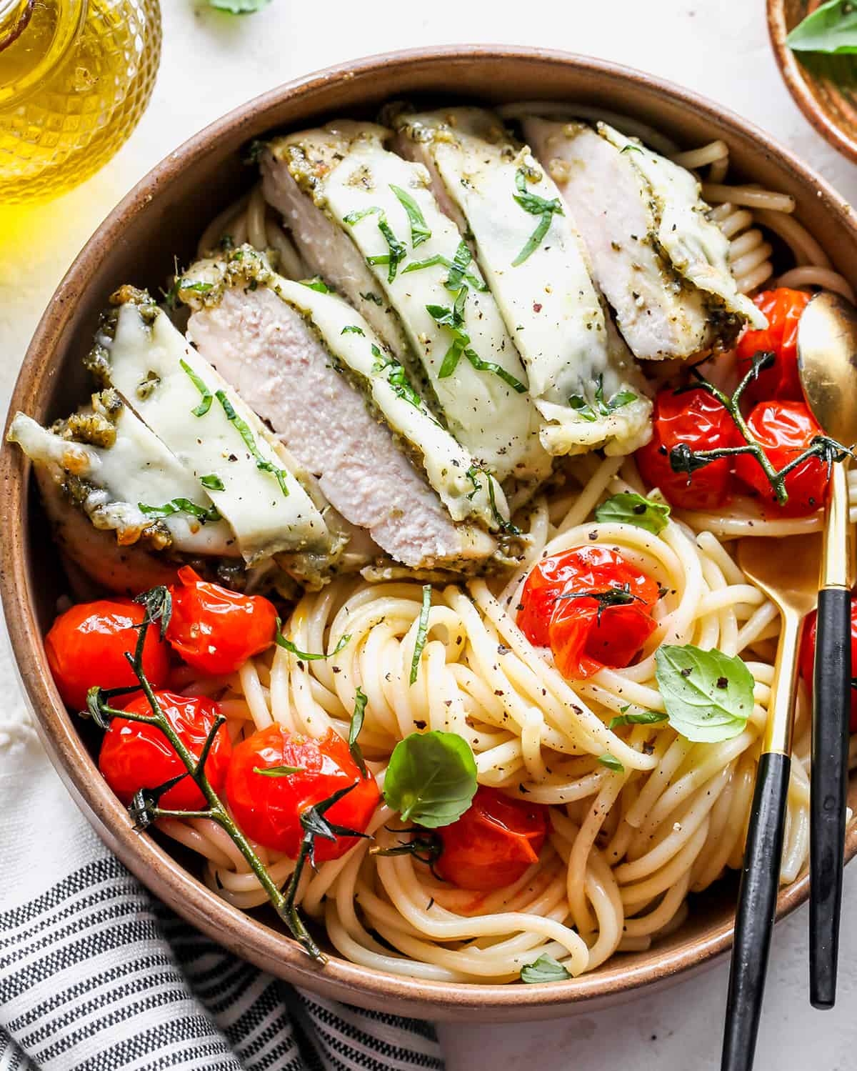Baked pesto chicken cut into slices over pasta with red tomatoes