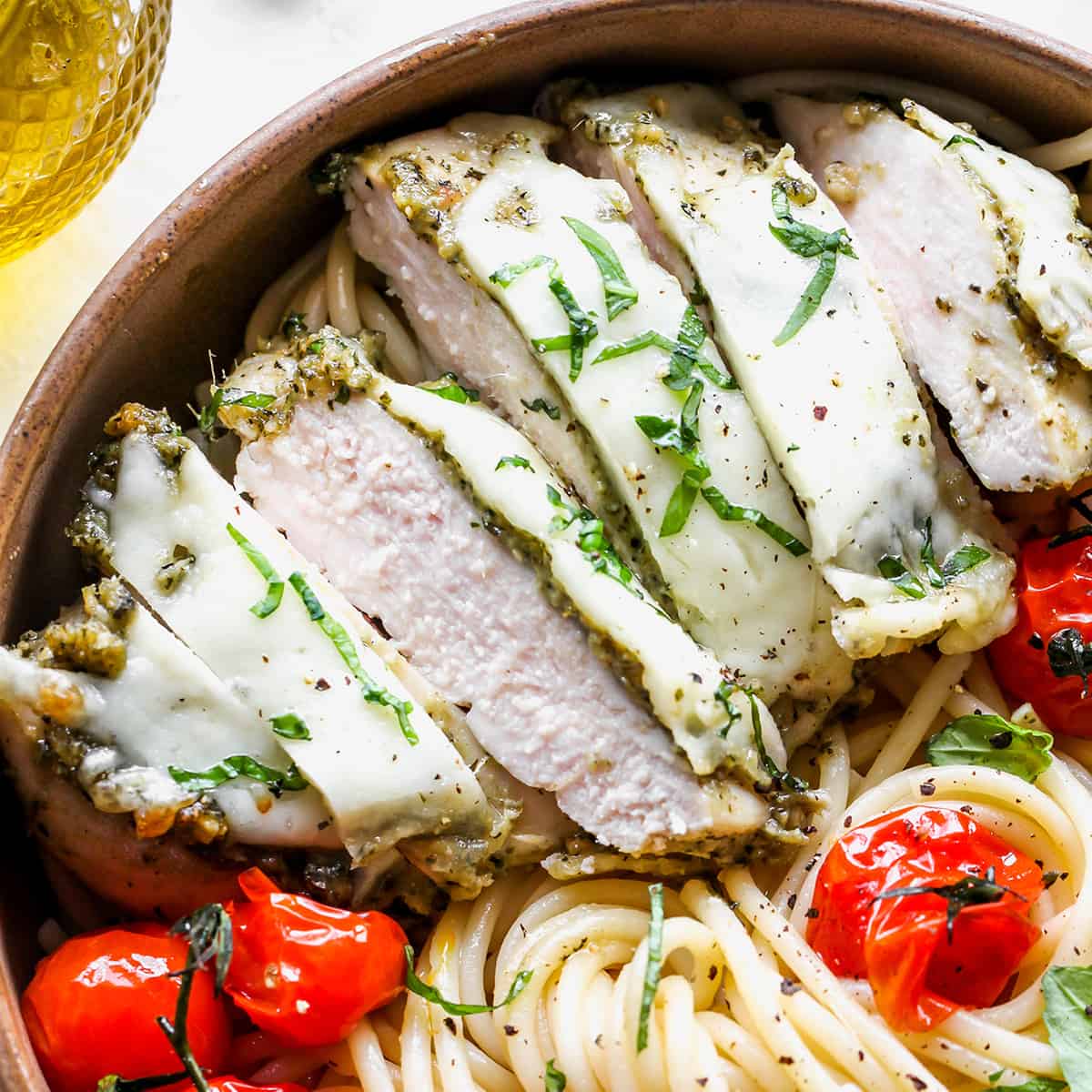 Baked pesto chicken cut into slices over pasta with red tomatoes