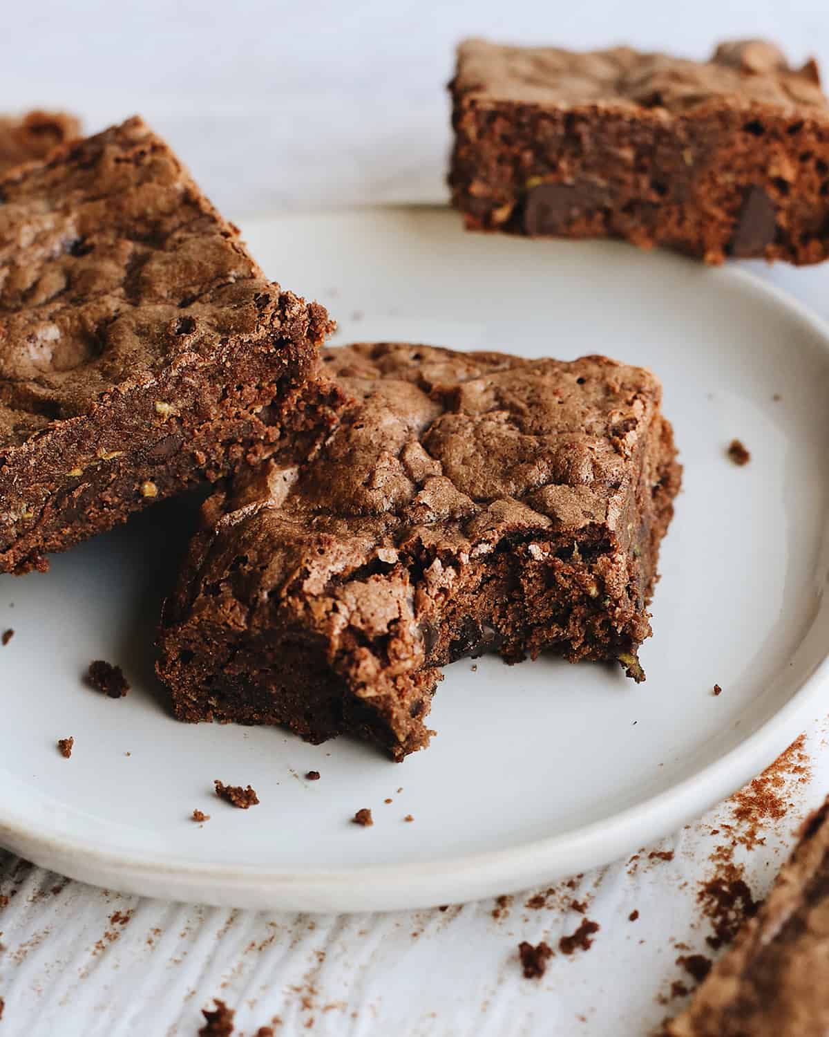 two chocolate zucchini brownies on a plate, one with a bite taken out of it
