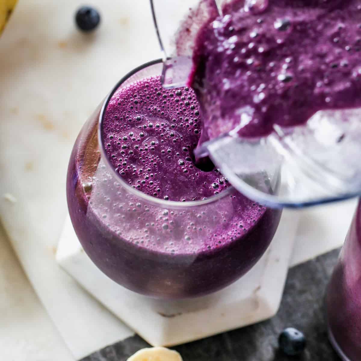 blueberry smoothie being poured from a blending container into a glass