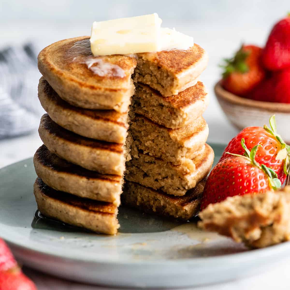 front view of a stack of 5 banana oat pancakes with butter and syrup and a piece cut out of the stack
