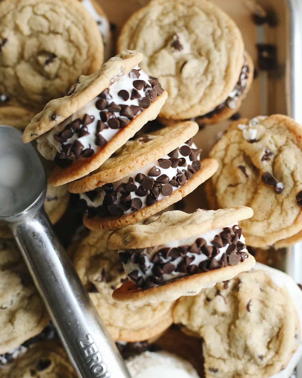 three chocolate chip cookie ice cream sandwiches laying on their sides on top of other cookie ice cream sandwiches. 