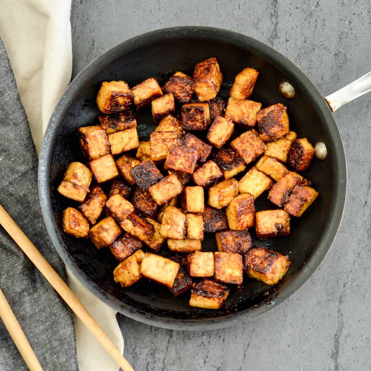 Overhead view of crispy tofu with hoisin sauce in a frying pan.