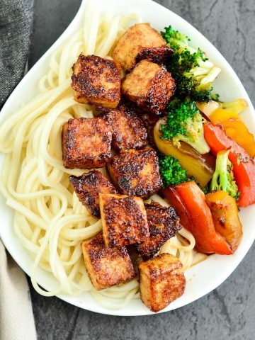 Overhead view of crispy tofu with hoisin sauce on a plate with noodles and stir fried veggies.