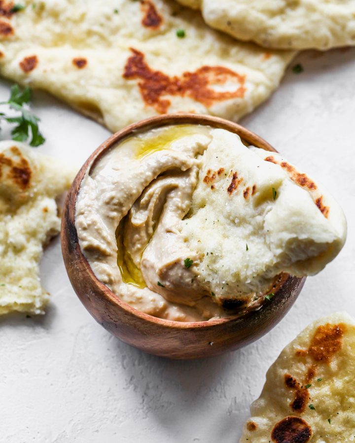 a piece of naan being dipped into a bowl of hummus