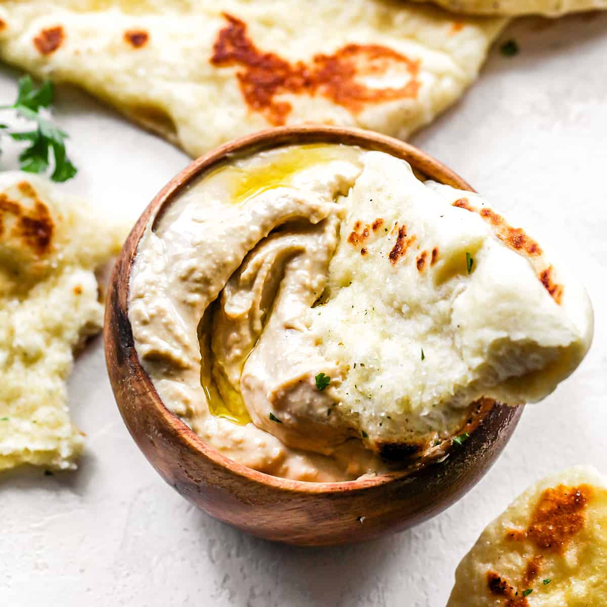a piece of naan being dipped into a bowl of hummus