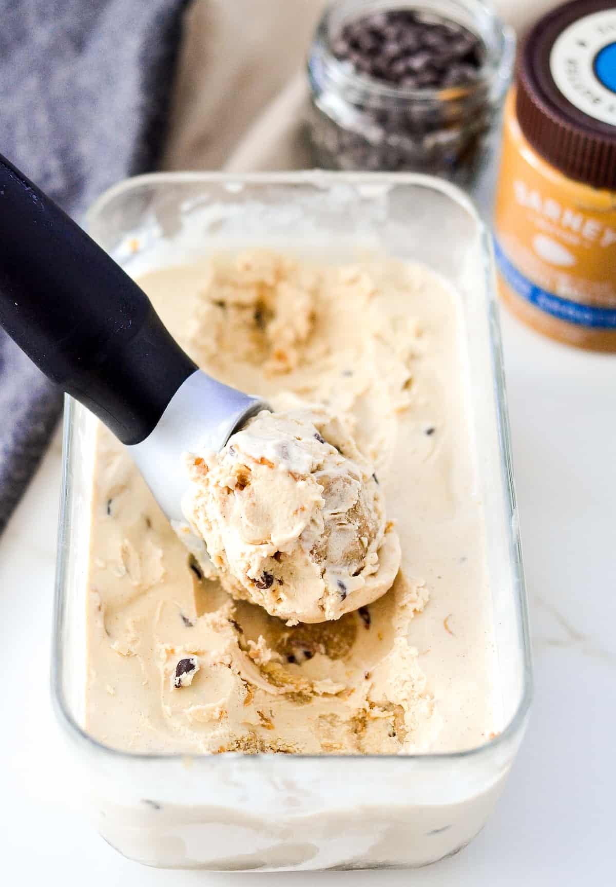 overhead/side view of a rectangular glass container of vegan & paleo cookie dough ice cream being scooped with an ice cream scoop