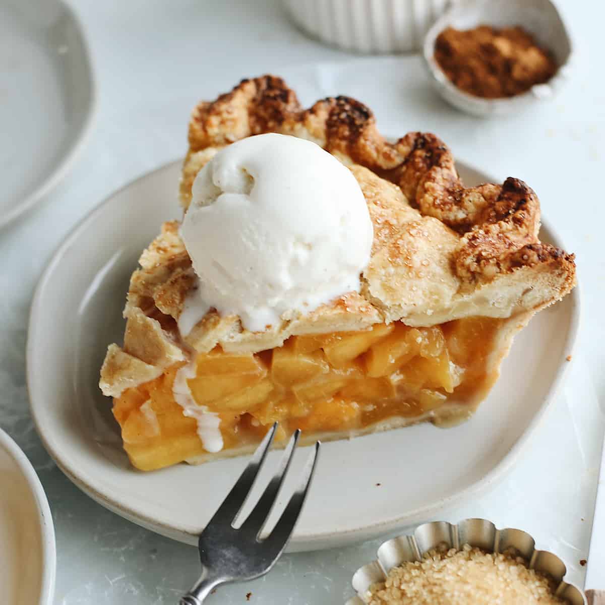 a piece of Fresh Peach Pie on a plate with a scoop of vanilla ice cream on top