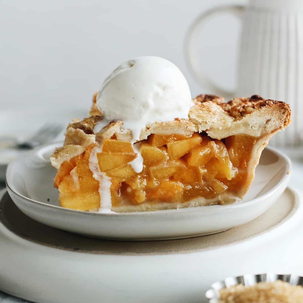 side view of a slice of peach pie on a plate with vanilla ice cream on top