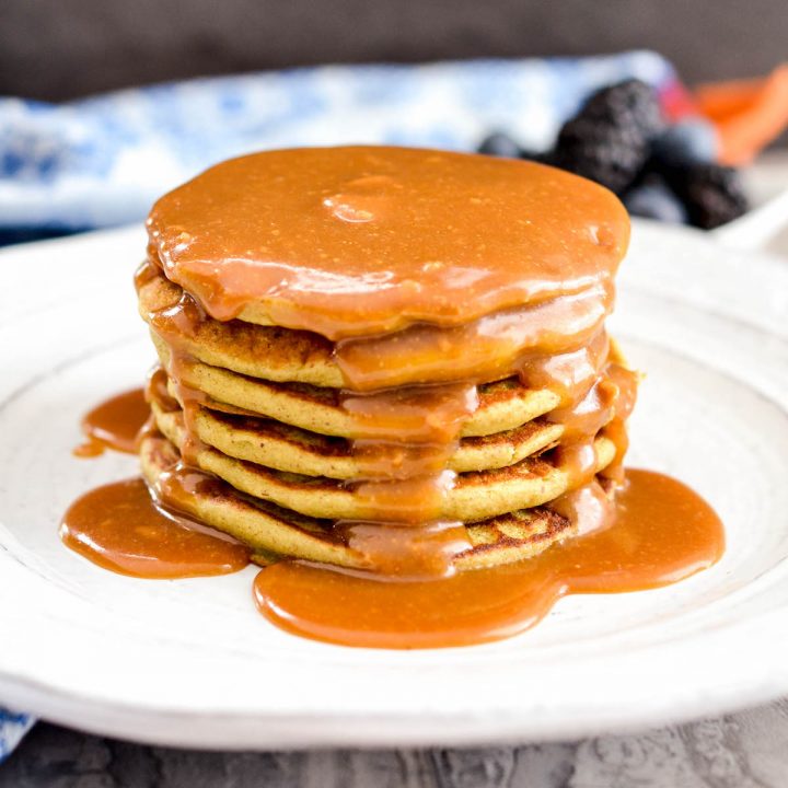 Front view of a stack of six Zucchini Banana Oatmeal Pancakes with maple syrup and peanut butter.