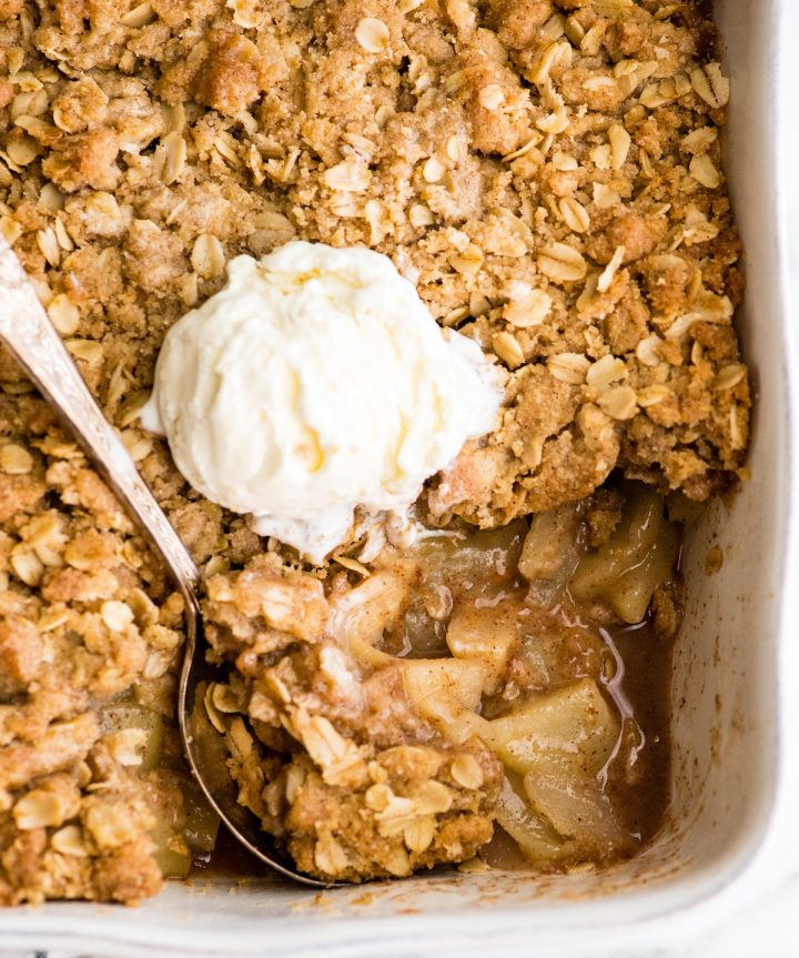 overhead view of apple crisp in a white baking dish after a scoop has been taken out, with a scoop of ice cream on top