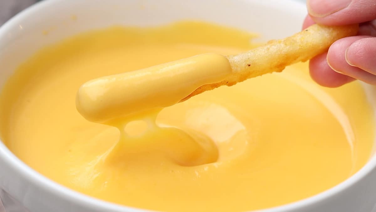 front view of a hand dipping a french fry in cheese sauce 