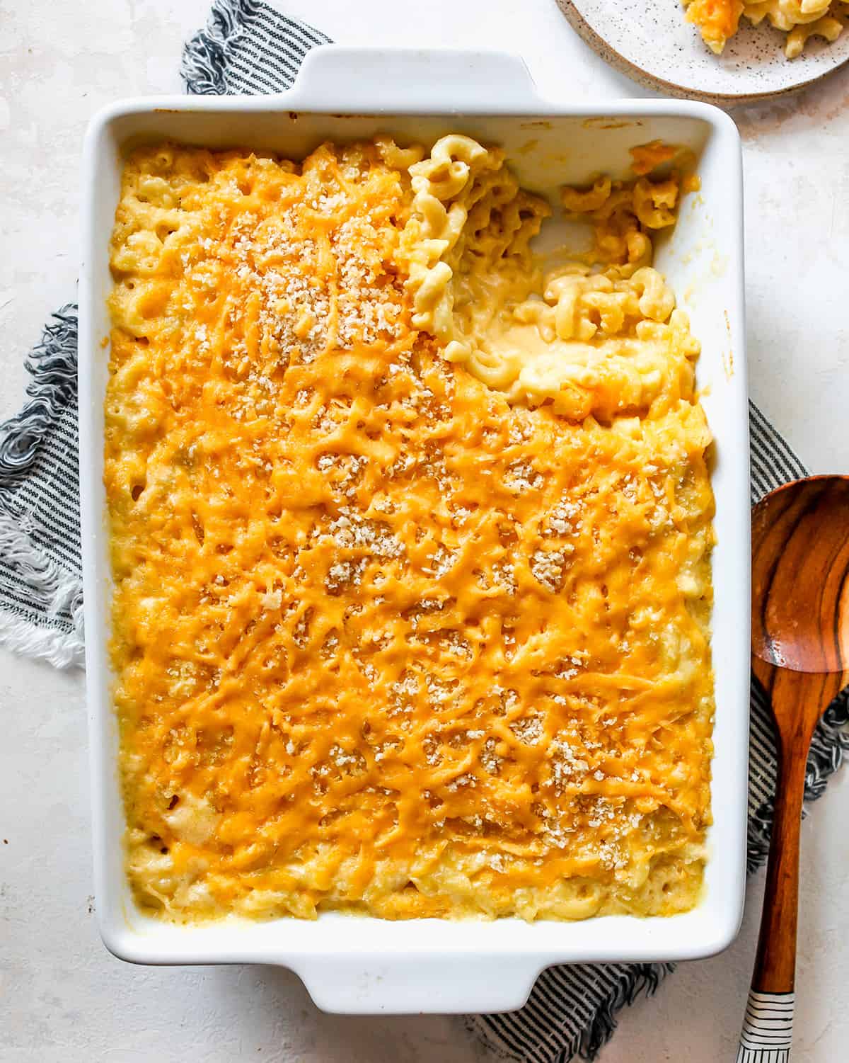 overhead photo of a white baking pan filled with baked macaroni and cheese, part of it scooped out onto a plate in the upper right hand corner.