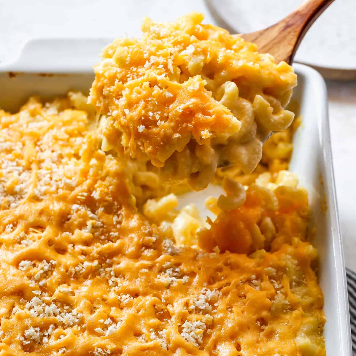 up close view of a wooden spoon scooping Baked Macaroni and Cheese out of a white baking dish