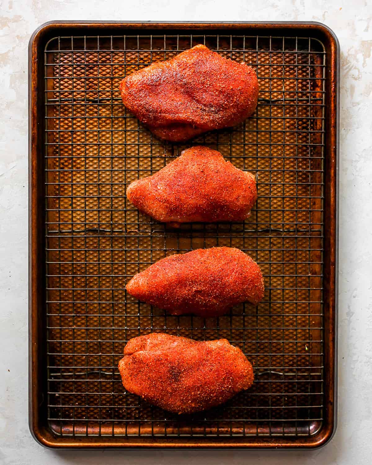 overhead photo showing how to cook chicken breasts in the oven - breasts coated with spice mixture on a wire rack on a baking sheet