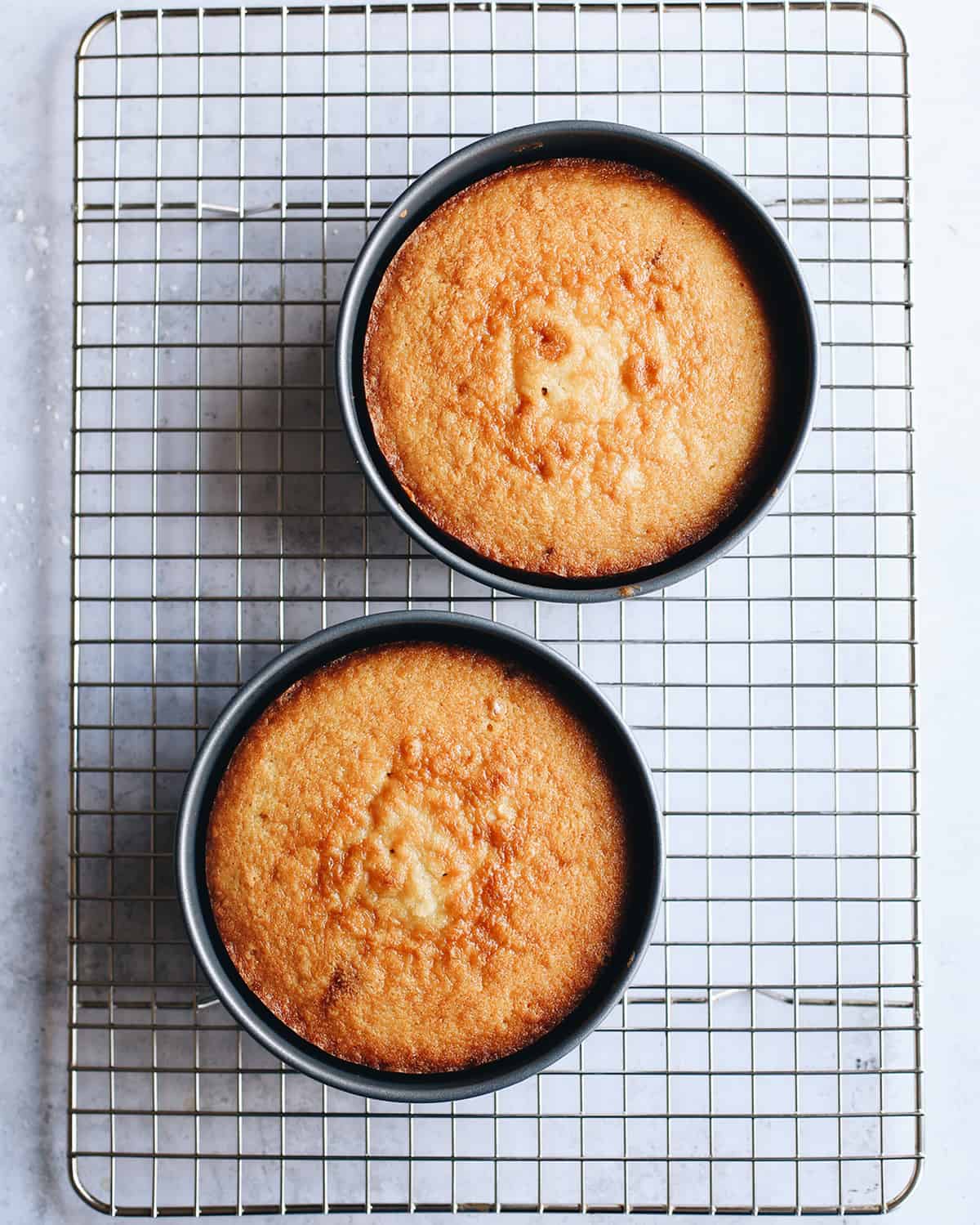 two yellow cakes in cake pans on a wire cooling rack 