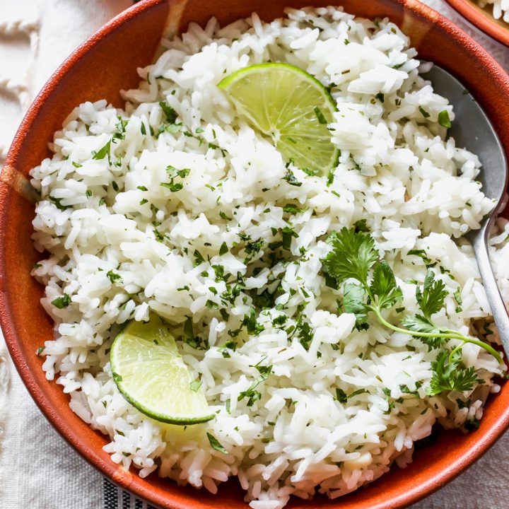 overhead view of a bowl of Cilantro Lime Rice garnished with cilantro and limes with a spoon in it