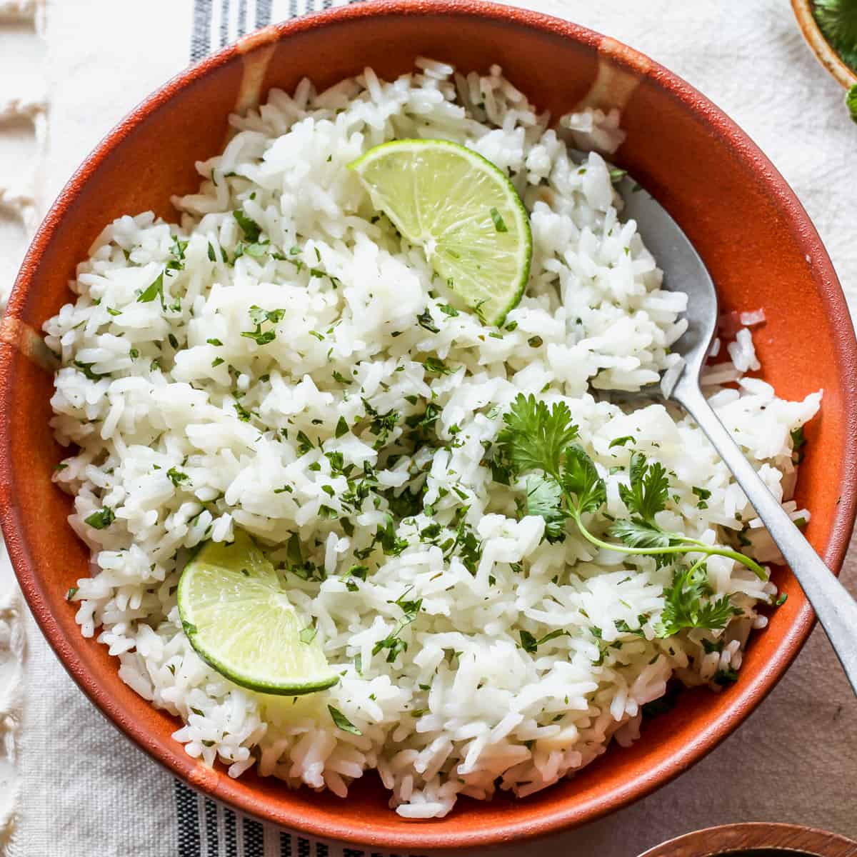 overhead view of a bowl of Cilantro Lime Rice garnished with cilantro and limes with a spoon in it