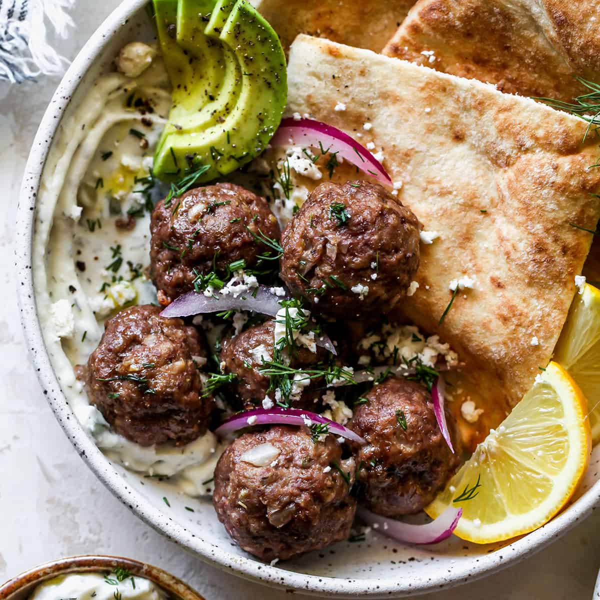 overhead view of Greek Meatballs in a bowl with tzatziki, pita, red onion, fresh dill and feta cheese