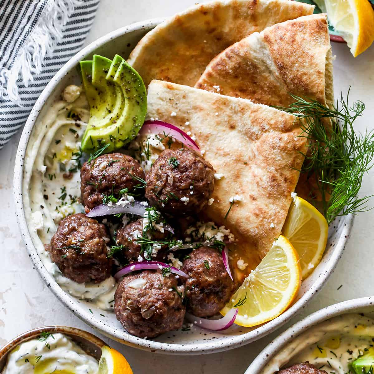 overhead view of Greek Meatballs in a bowl with tzatziki, pita, red onion, fresh dill, avocado and feta cheese