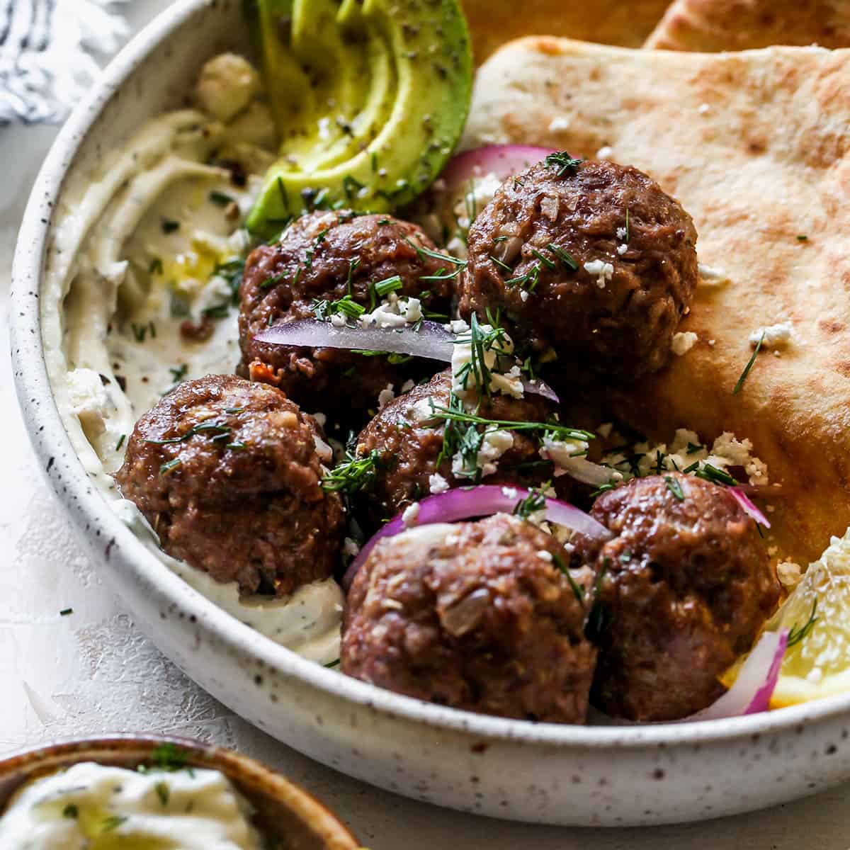 font view of Greek Meatballs in a bowl with tzatziki, pita, red onion fresh dill, avocado and feta cheese