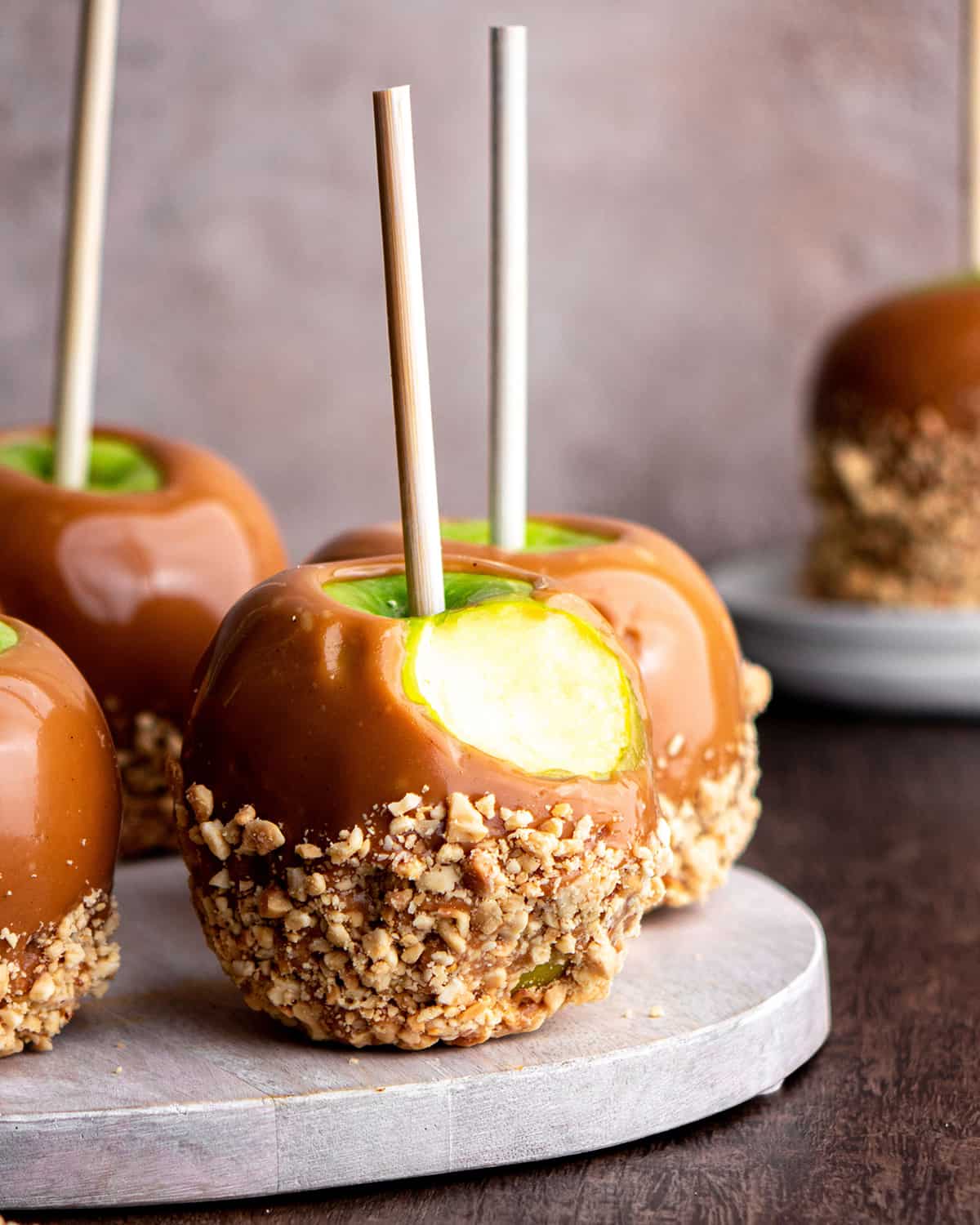 front view of 4 Homemade Caramel Apples, one has a bite taken out of it 