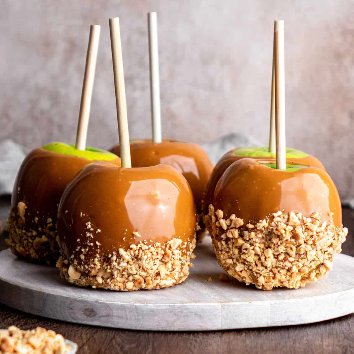 front view of 5 Homemade Caramel Apples on a round wooden serving board 