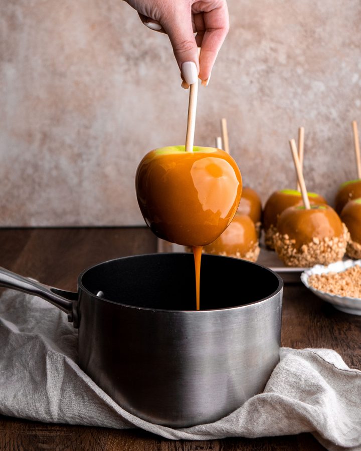front view of an apple being dipped in caramel in a pot 