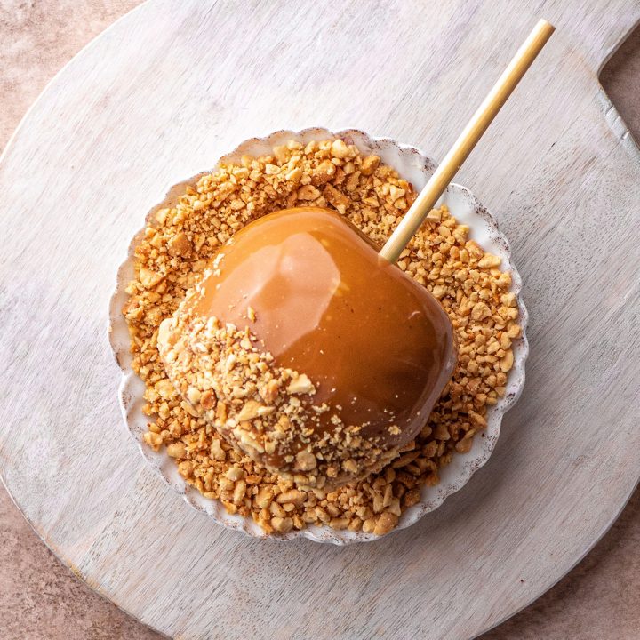 overhead view of a Homemade Caramel Apple being rolled in crushed peanuts