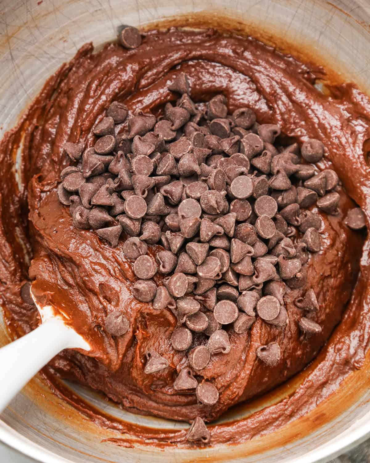 chocolate chips added to the pumpkin brownie batter in a metal mixing bowl before mixing in. A spatula is in the batter too. 