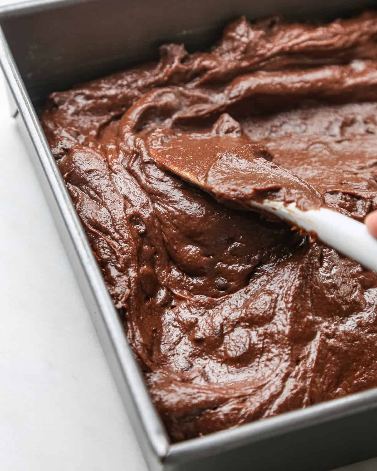 pumpkin brownies batter being spread into a metal baking dish