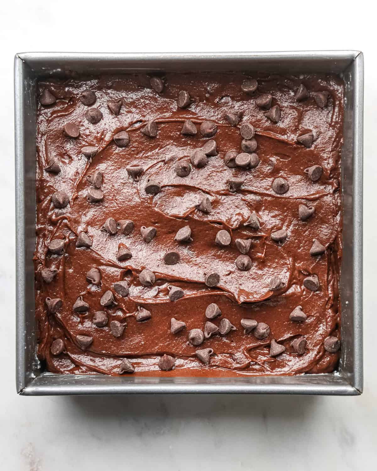 pumpkin brownies in a square metal baking pan topped with chocolate chips before baking