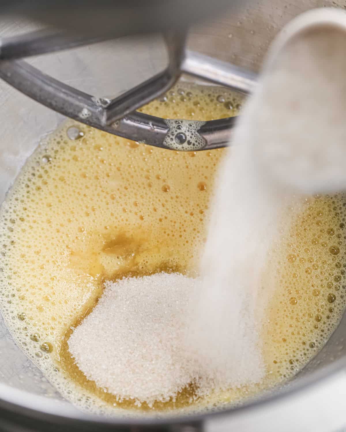 making pumpkin brownies - sugar being poured into the beaten egg mixture in a metal mixing bowl