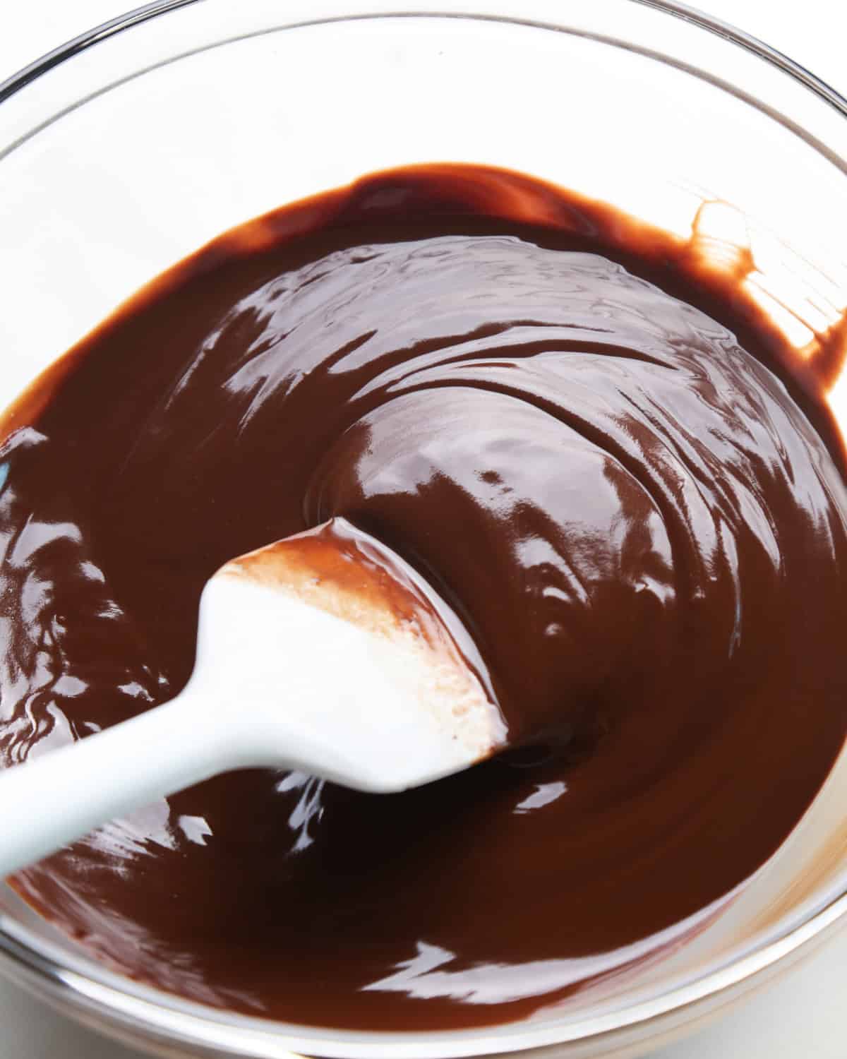making pumpkin brownies - melted chocolate and butter in a glass bowl with a spatula in the chocolate mixture showing its texture