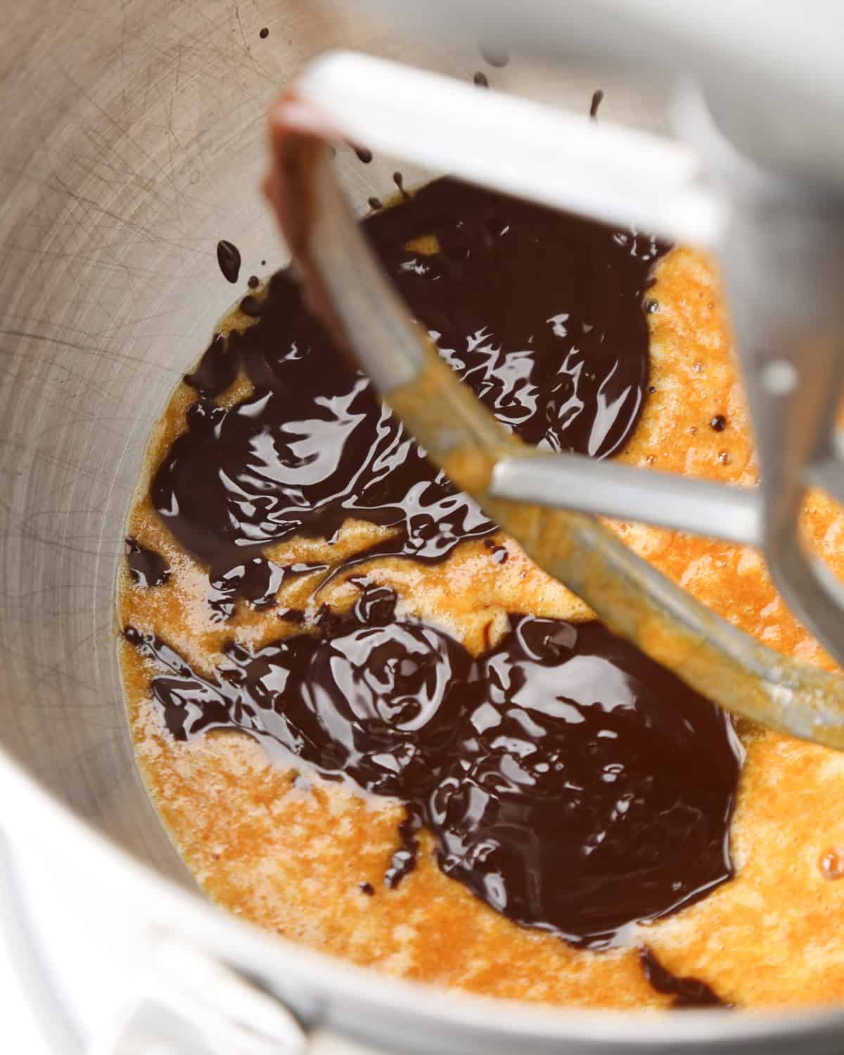 melted chocolate and butter mixture added to the pumpkin brownies batter in a metal mixing bowl with a gray paddle attachment