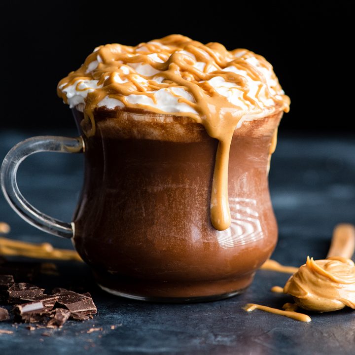 a glass mug filled with Peanut Butter Hot Chocolate topped with whipped cream and a drizzle of peanut butter