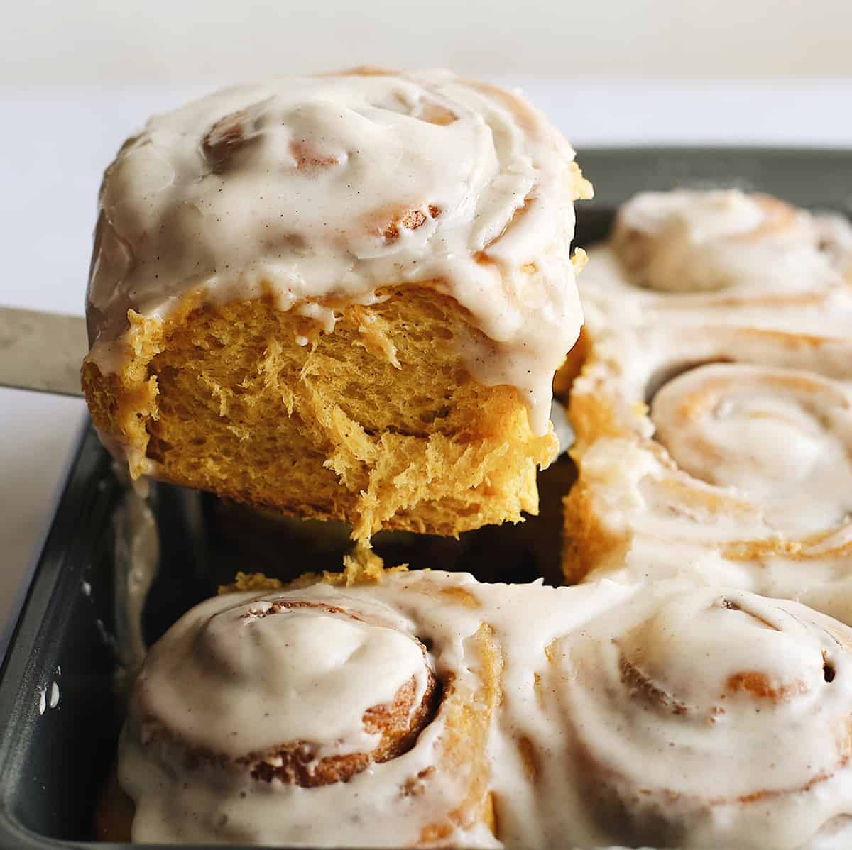 a Pumpkin Cinnamon Roll being lifted out of the pan with a spatula