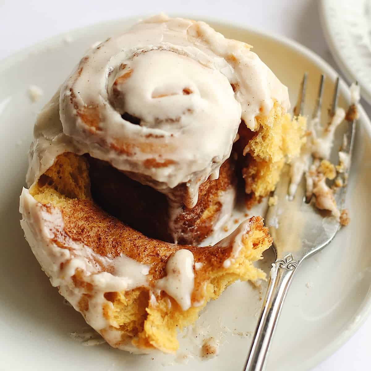 up close photo of a pumpkin cinnamon roll on a plate with a fork