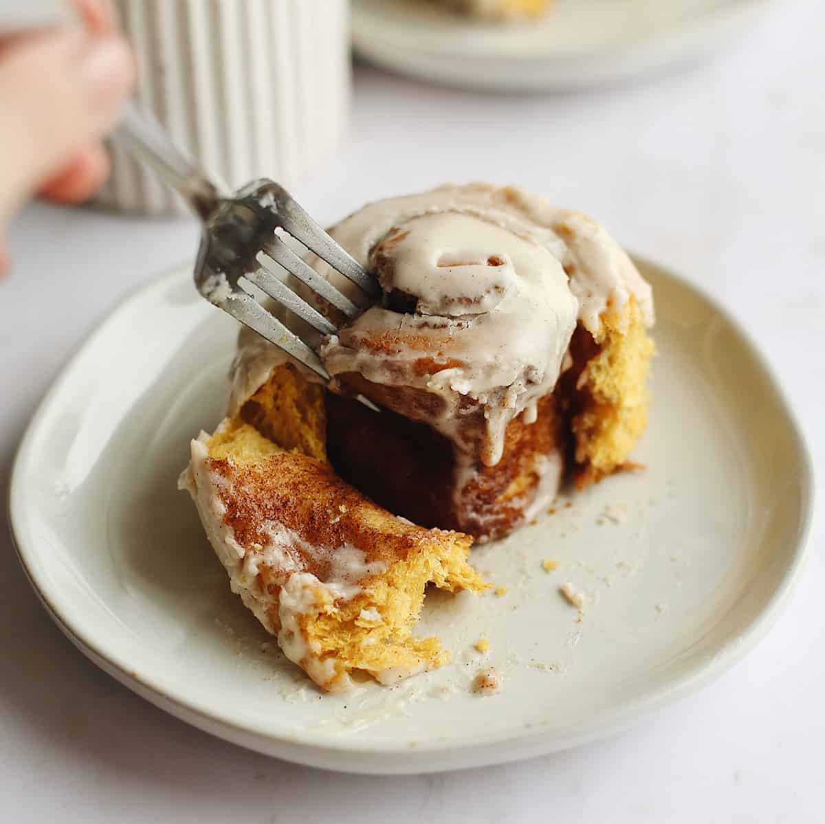a fork taking a bite out of a Pumpkin Cinnamon Roll on a plate