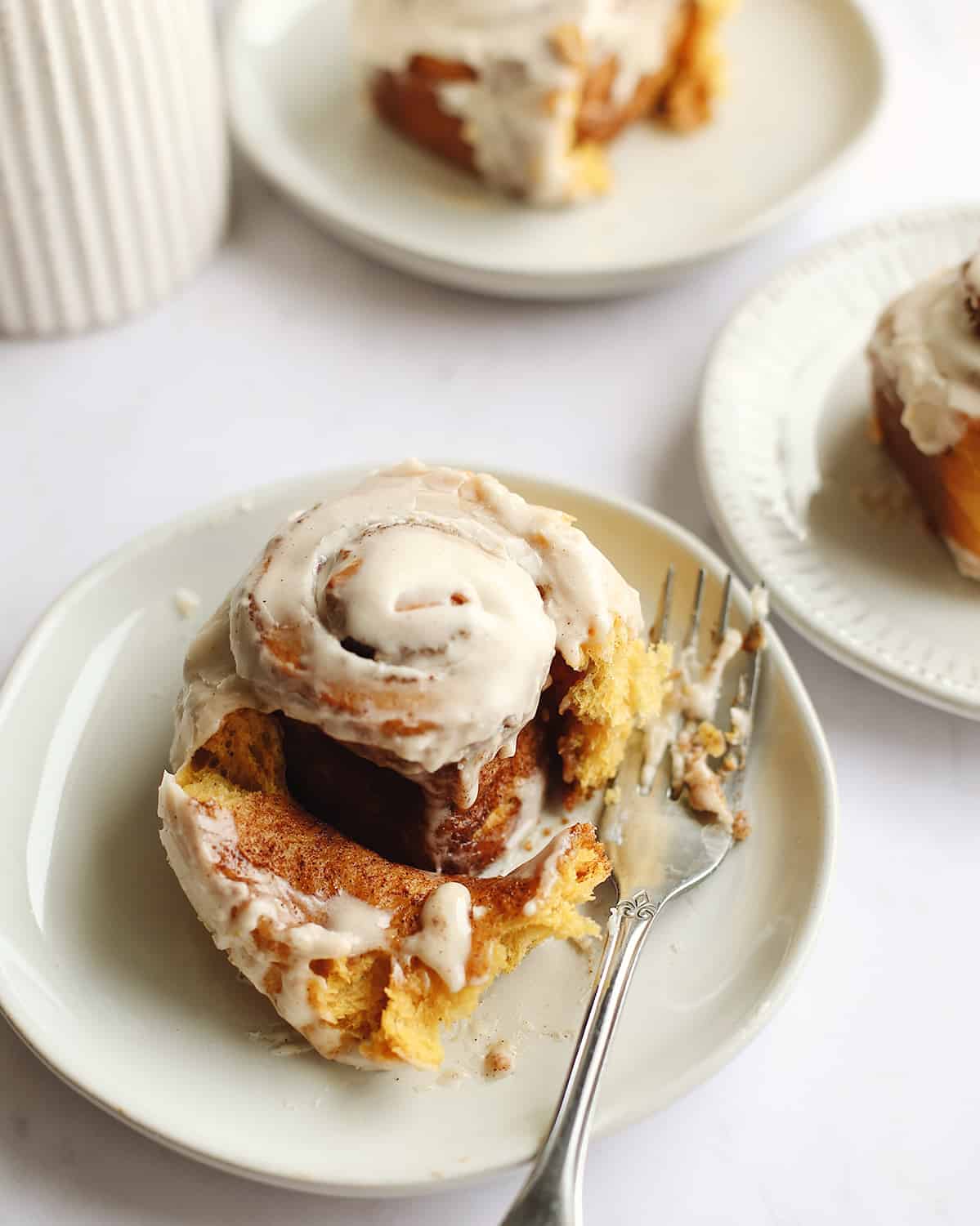 pumpkin cinnamon roll on a plate with a bite taken out of it and a fork next to it