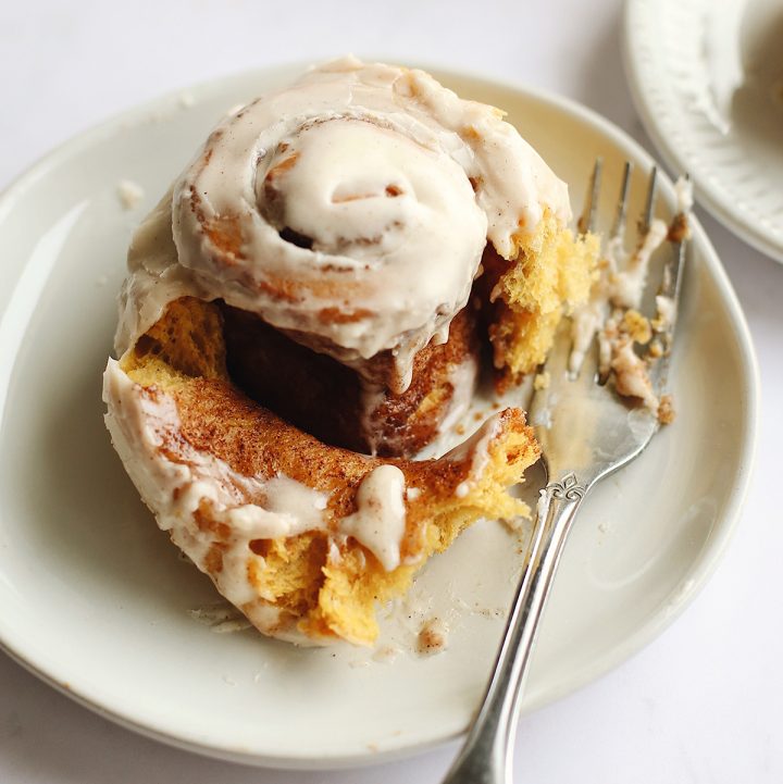 pumpkin cinnamon roll on a plate with a bite taken out of it and a fork next to it
