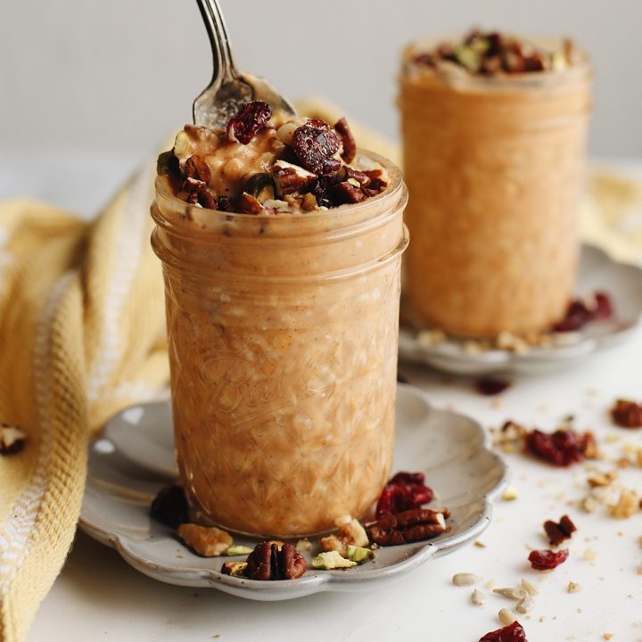 front view of two glass jars of Pumpkin Overnight Oats topped with nuts, one has a spoon in it