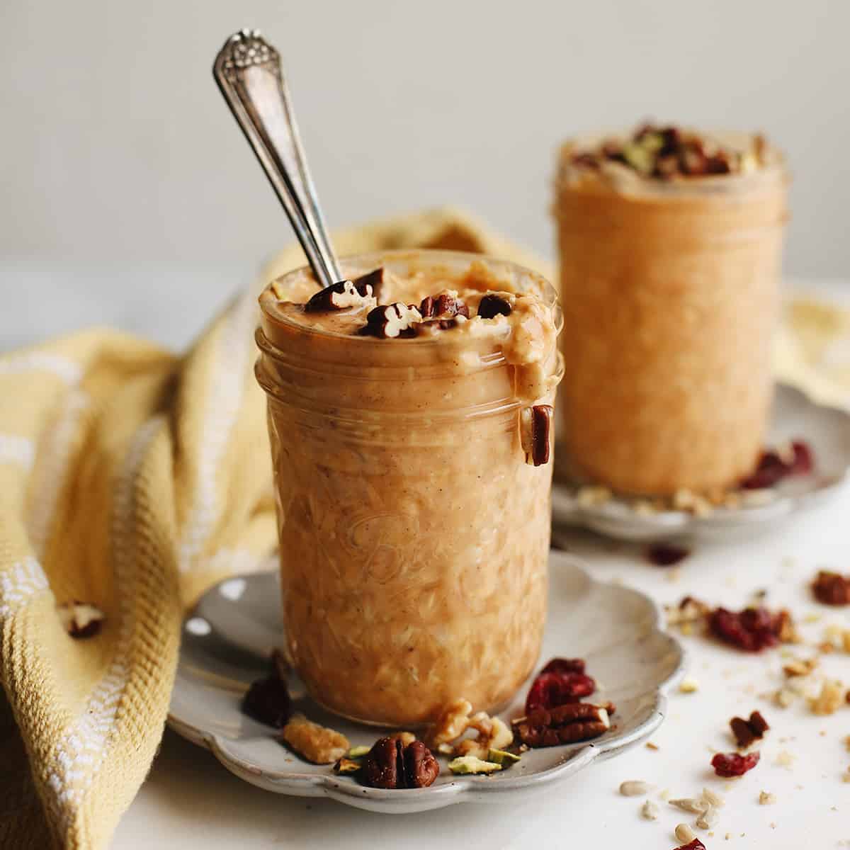 front view of two glass jars of Pumpkin Overnight Oats topped with nuts, one has a spoon in it
