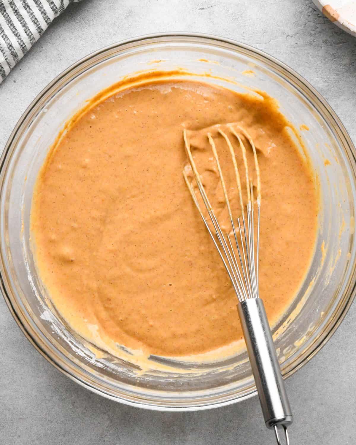 making pumpkin pancakes recipe - final pumpkin pancakes batter in a glass bowl with a metal wire whisk.