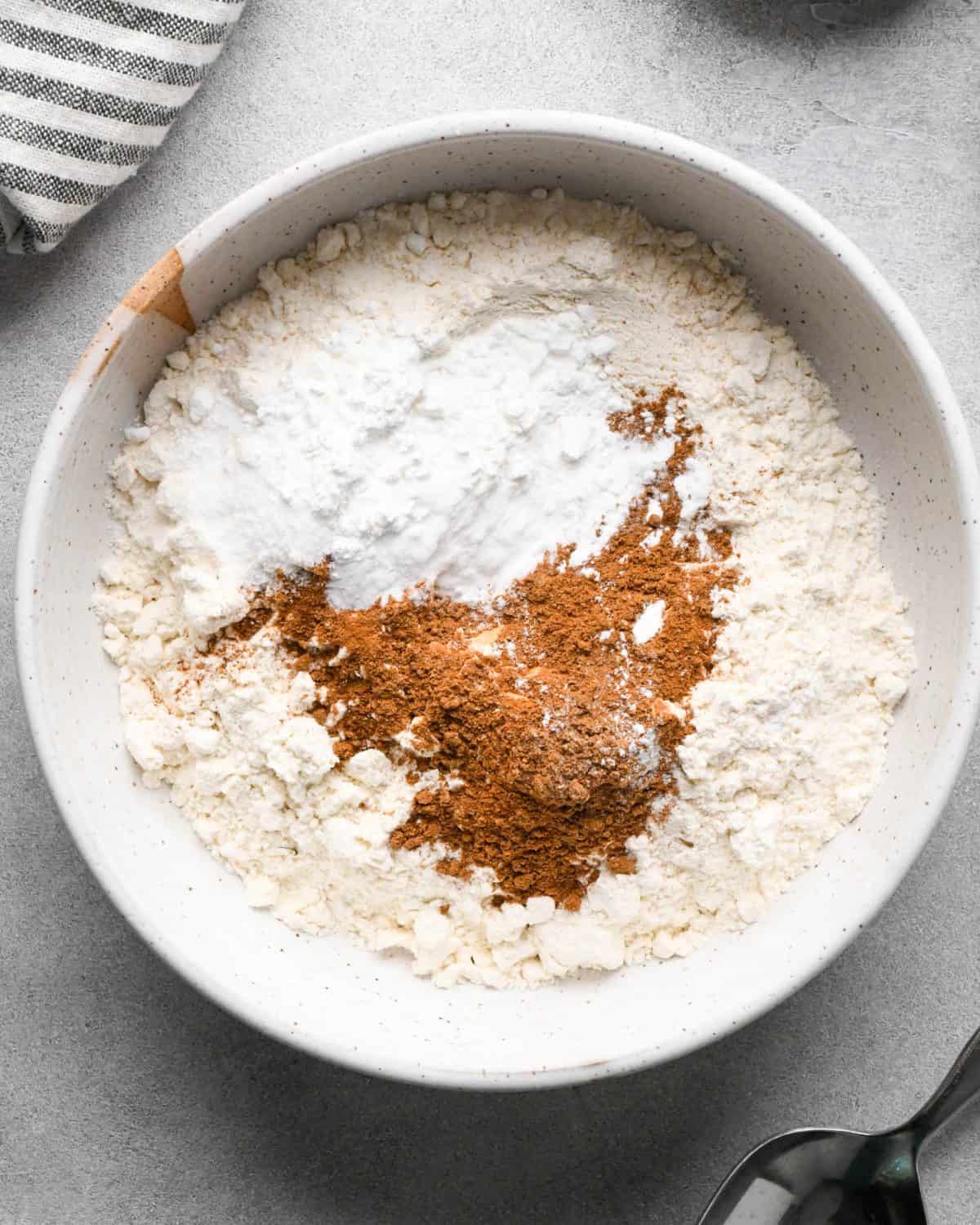 making pumpkin pancakes recipe - flour, baking powder, baking soda, salt, cinnamon and pumpkin pie spice in a small white ceramic bowl before mixing