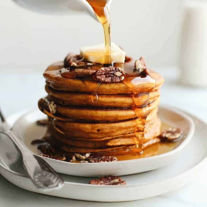 a stack of 6 Pumpkin Pancakes with butter and pecans and maple syrup being poured on top