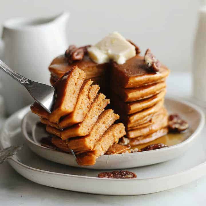 a fork holding a bite of Pumpkin Pancakes in front of a stack of Pumpkin Pancakes