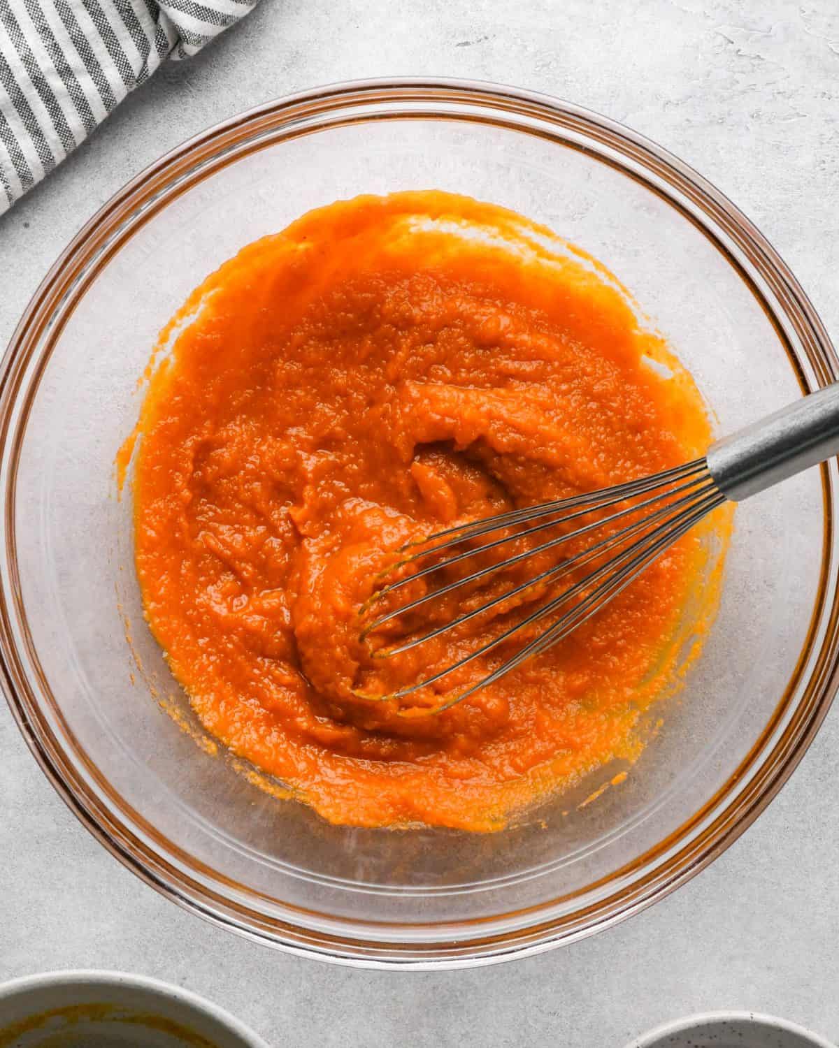 making pumpkin pancakes recipe - pumpkin puree and white sugar in a glass bowl whisked together with a metal whisk