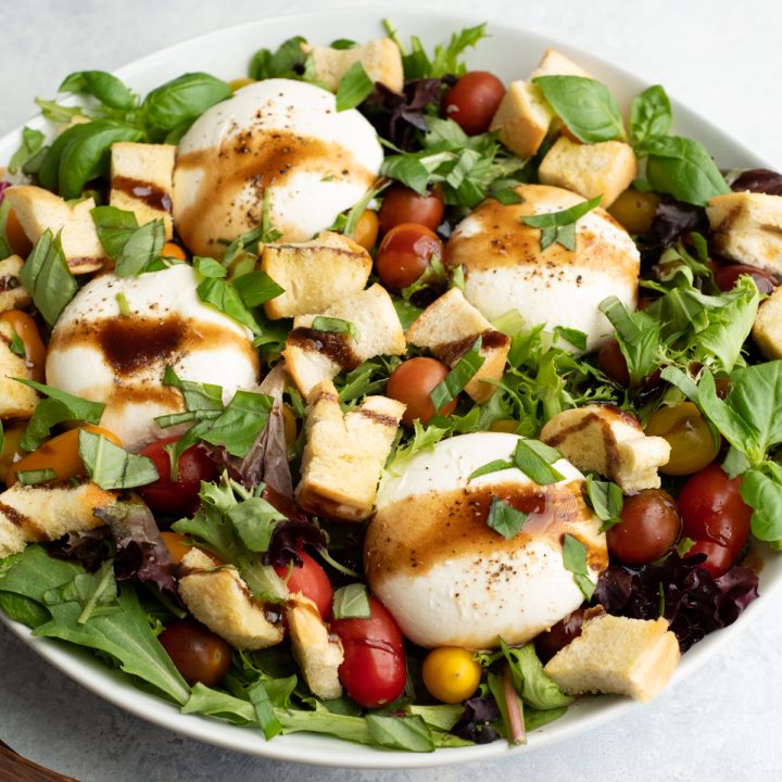 burrata salad in a large white serving dish drizzled with balsamic vinaigrette