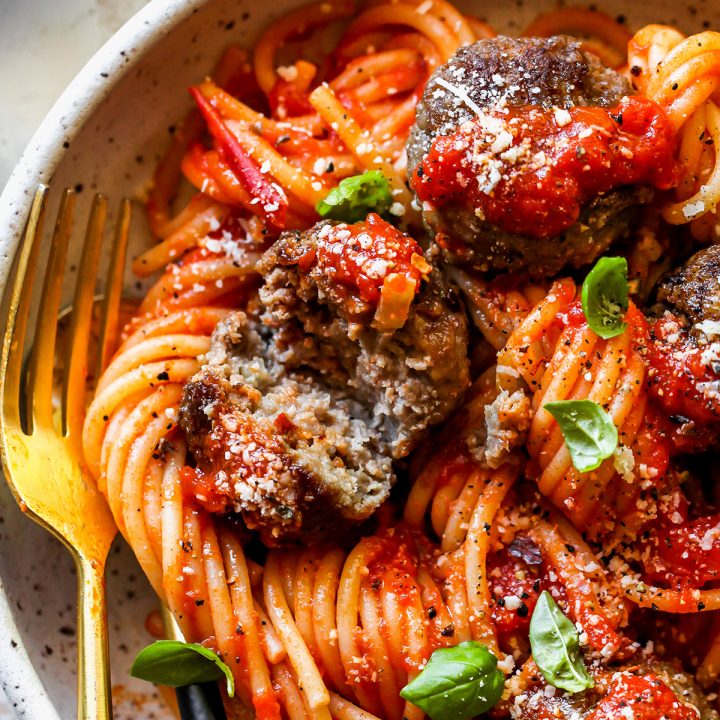 a homemade meatball cut in half served over pasta in marinara sauce garnished with basil